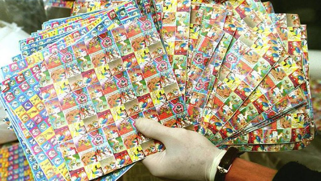 Vibrant stack of colorful LSD blotter sheets with intricate cartoon and psychedelic designs – iconic representation of traditional blotter form in the history and origins of LSD.