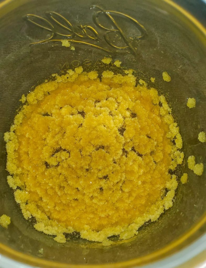 Close-up of exquisite pure yellow DMT crystals forming stunning flower-like clusters in jar – showcasing the radiant beauty and superior quality of high-grade N,N-DMT.