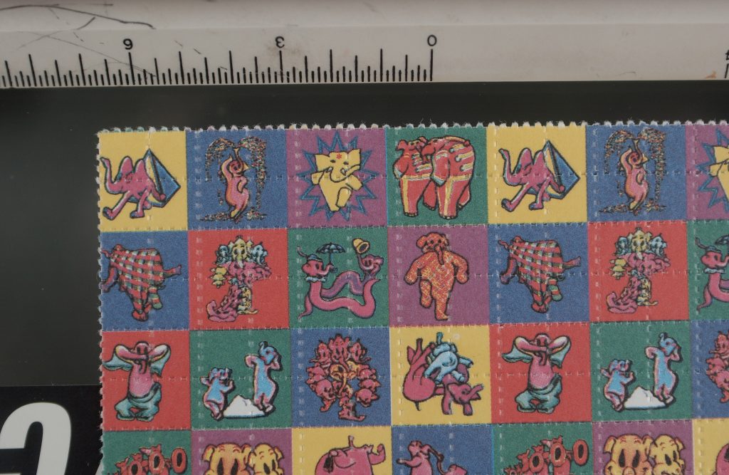 A full sheet of colorful artisanal LSD blotter art featuring elephants and animals, shown next to a ruler for scale and precision verification.