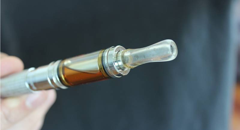 A high-quality glass and metal DMT vape cartridge held up to show clear, lab-tested oil and professional hardware.
