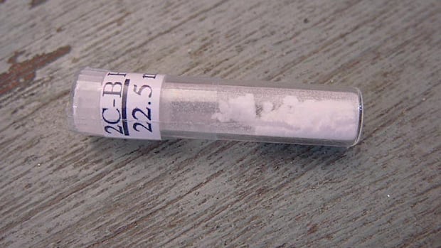 An analytical glass vial displaying a 22.5 mg label of 2C-B powder compared against pressies to demonstrate exact volumetric dosing uniformity.