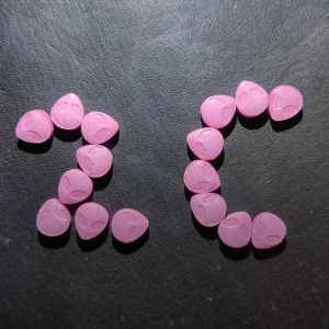 Pink alien-shaped compressed 2C-B Pills arranged to spell out 2C on a dark textured surface.