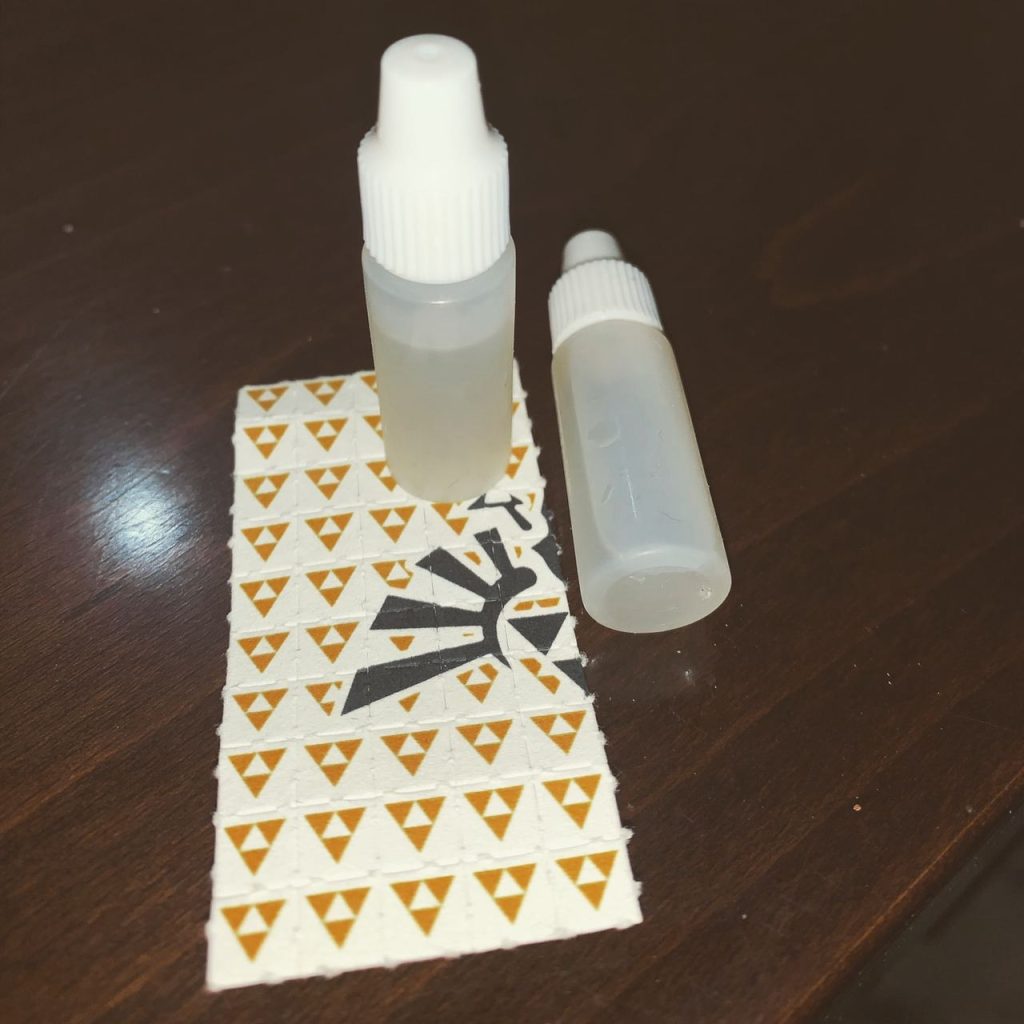Two calibrated translucent dropper bottles containing liquid solutions alongside a classic perforated paper sheet.