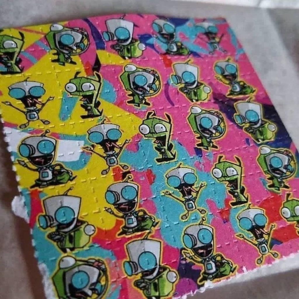 A perforated sheet of colorful art-printed LSD Blotters highlighting the textured cellulose paper matrix.
