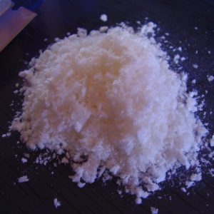 A high-purity mound of white isolated Mescaline HCl crystalline flakes on a dark laboratory surface.