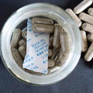 A top-down view of a clear glass jar filled with premium Psilocybin Mushroom Capsules and a protective silica desiccant packet.