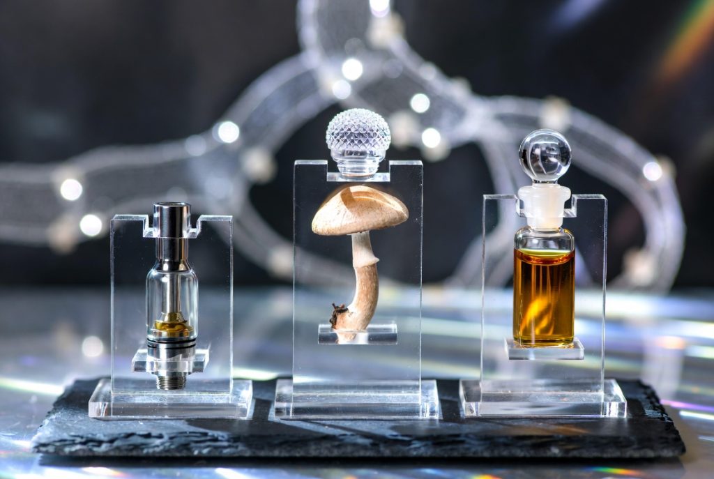 What is the closest drug to DMT showing a vape cartridge, magic mushroom, and amber liquid vial on display stands